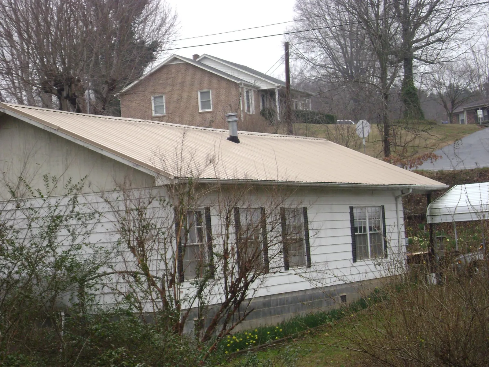 Tan metal roof on a white sided house set into a hillside — Commercial Roofing by Roofing Brothers in Erie