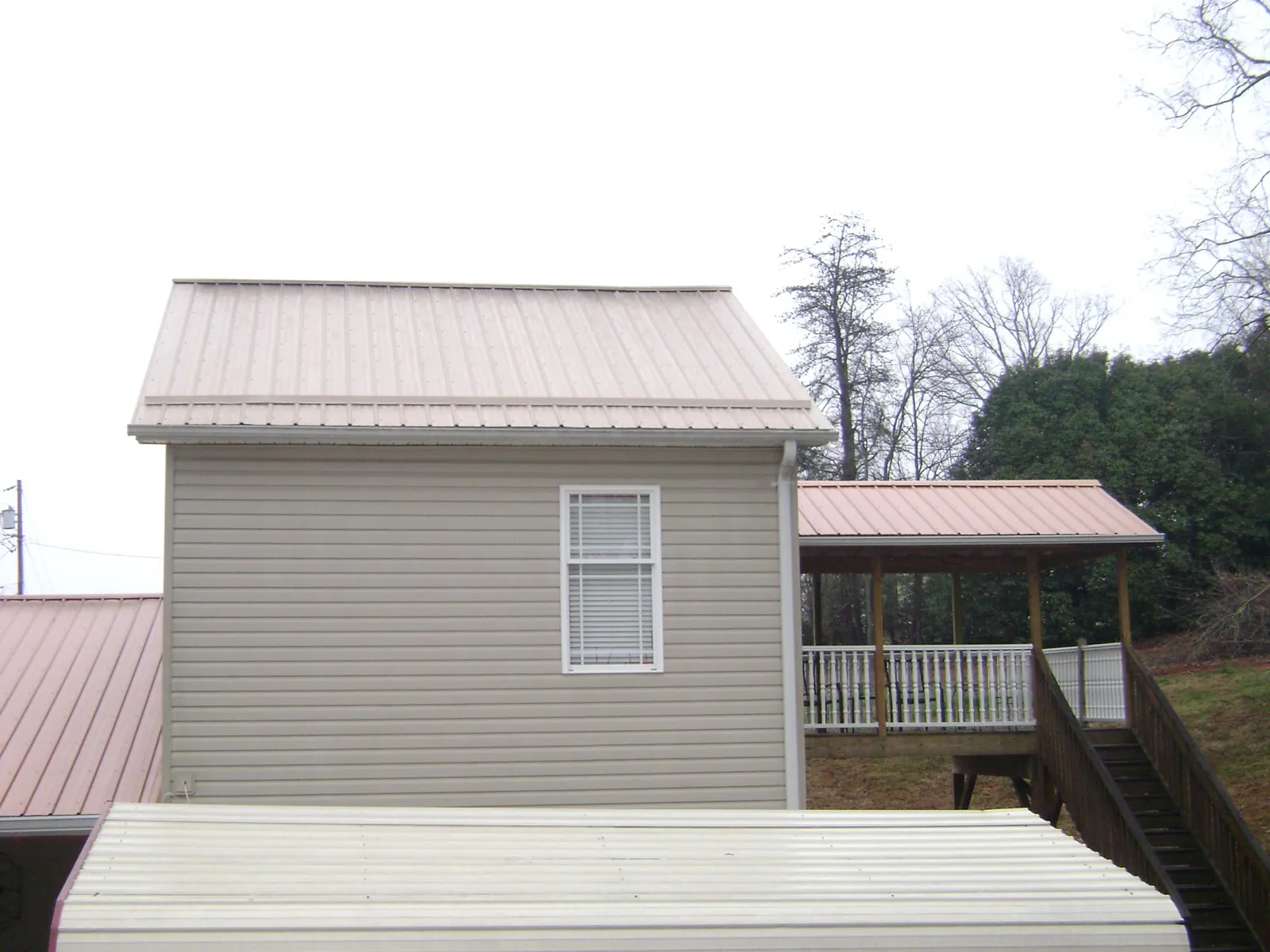 Tan metal roofs on a two story addition and attached porch, from a Roof Replacement job in Erie